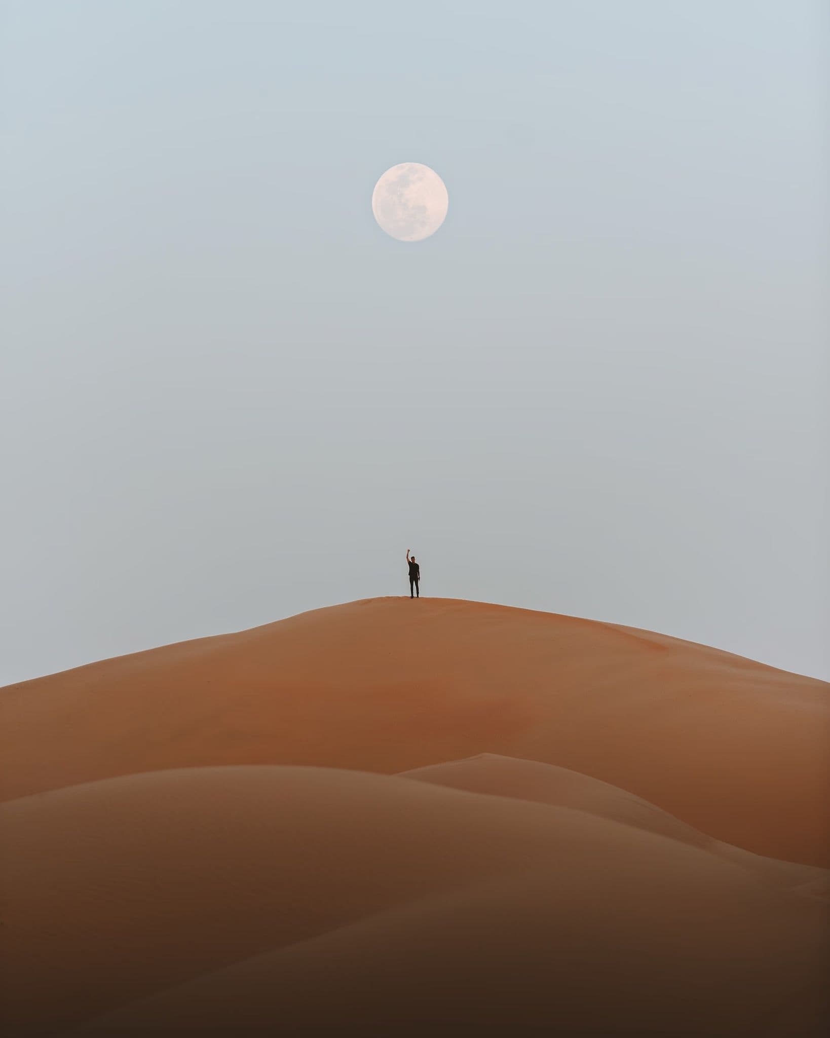 Person standing on a sand dune under a full moon.